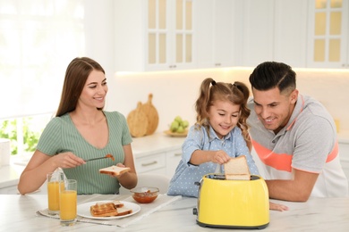 Photo of Happy family having breakfast with toasted bread at table in kitchen