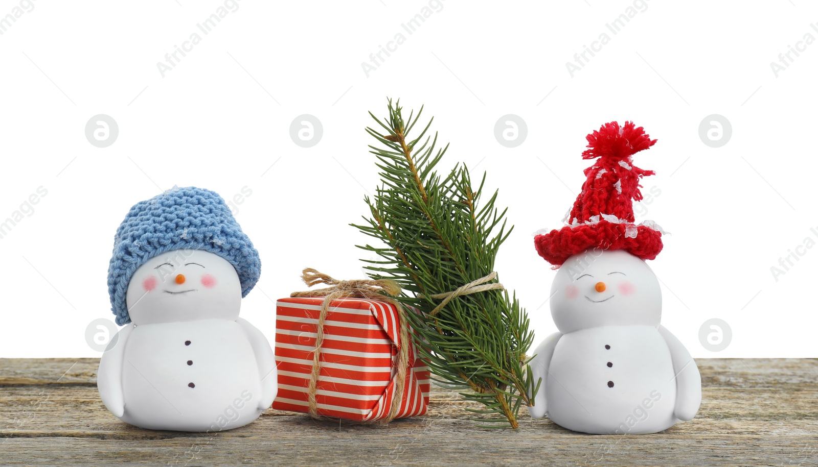 Photo of Cute decorative snowmen, gift box and fir tree branches on wooden table against white background