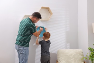 Photo of Father and son installing shelves on wall at home. Repair work