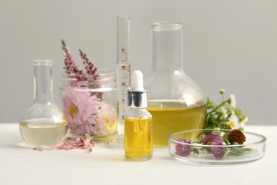 Photo of Cosmetic oil, laboratory dishware and flowers on white table