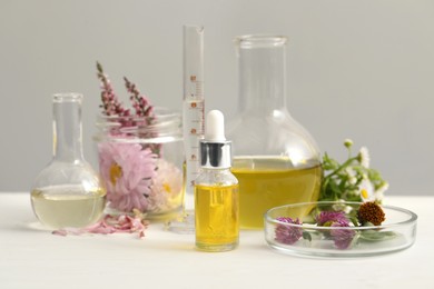 Cosmetic oil, laboratory dishware and flowers on white table