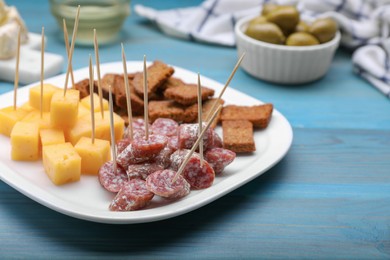 Photo of Toothpick appetizers. Pieces of sausage, cheese and croutons on light blue wooden table, closeup. Space for text