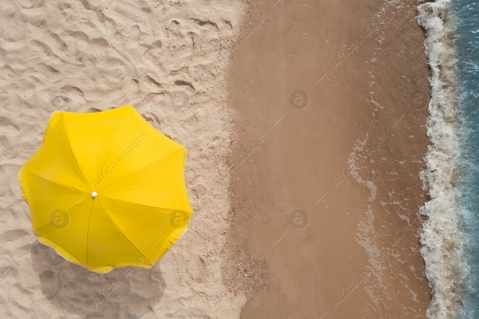 Image of Yellow beach umbrella on sandy coast near sea, top view