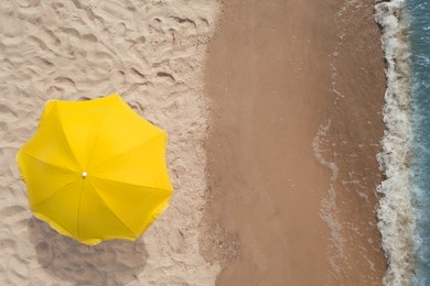 Yellow beach umbrella on sandy coast near sea, top view