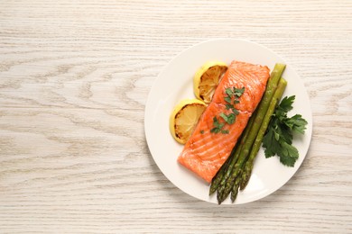 Photo of Tasty grilled salmon with asparagus and lemon on white wooden table, top view. Space for text