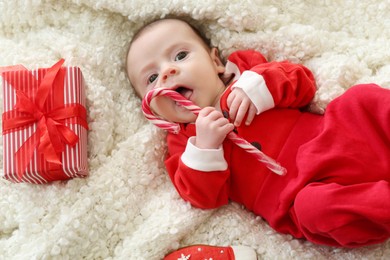 Cute little baby eating Christmas candy cane on soft blanket, top view
