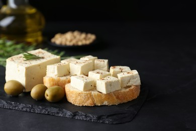 Pieces of delicious tofu with bread, rosemary and olives on black table. Soybean curd