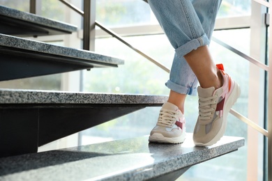 Photo of Young woman wearing stylish sneakers on grey stairs indoors, closeup