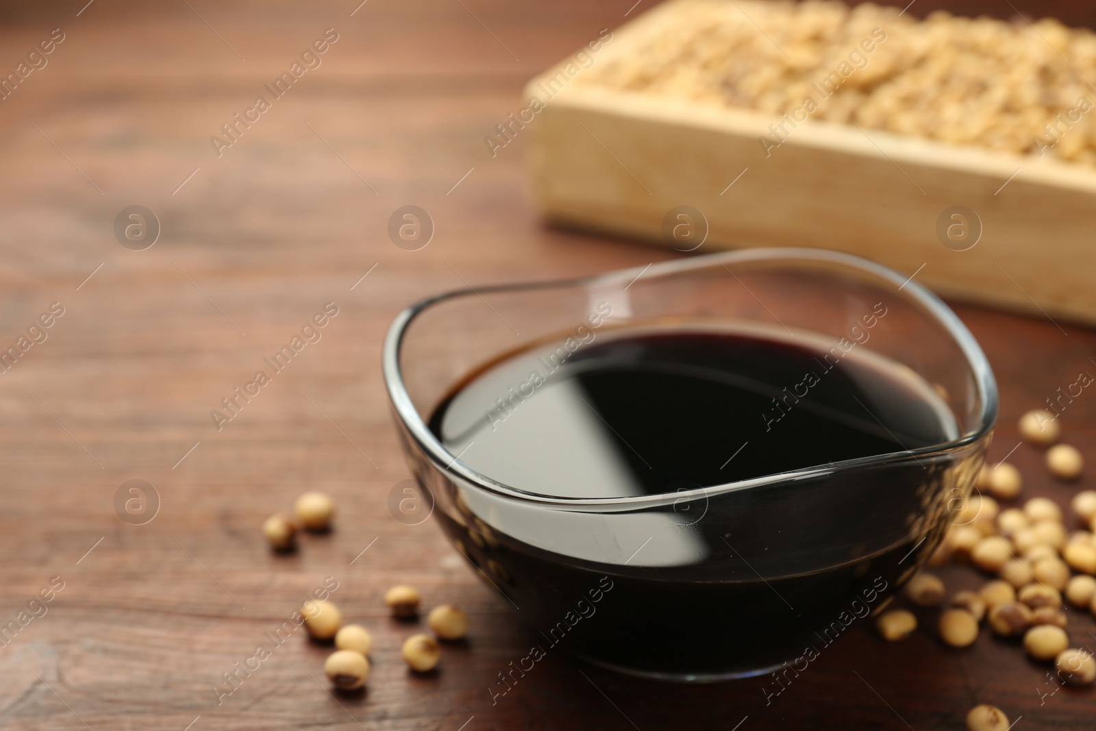 Photo of Soy sauce in bowl and soybeans on wooden table, closeup. Space for text