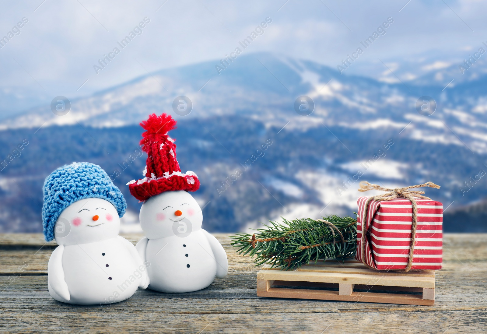 Image of Cute decorative snowmen, gift box and fir tree branches on wooden table in mountains