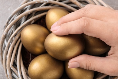 Woman taking golden egg from nest, closeup