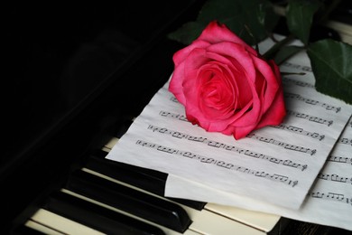 Photo of Beautiful pink rose and musical notes on piano keys, closeup
