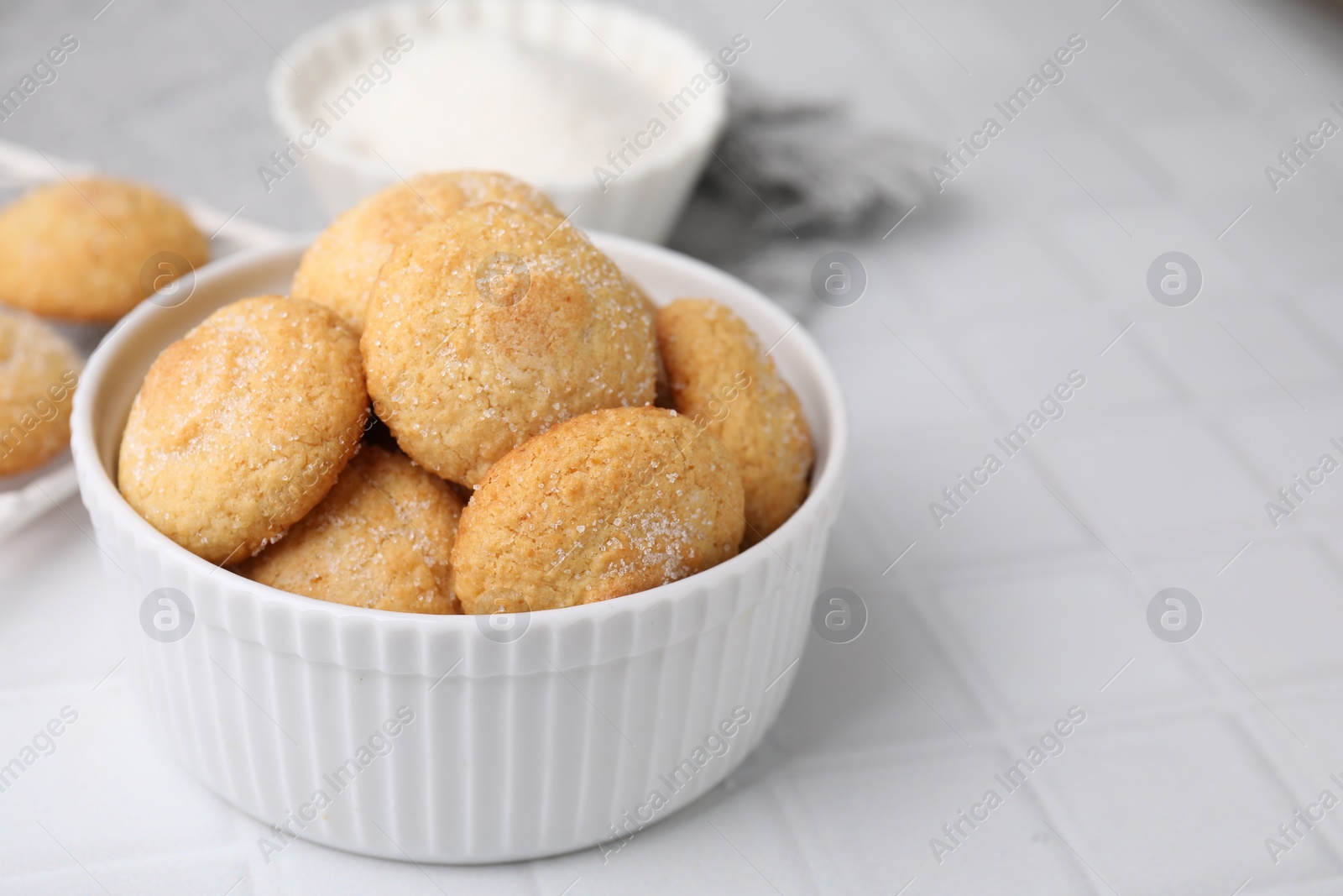 Photo of Tasty sugar cookies in bowl on white tiled table, closeup. Space for text