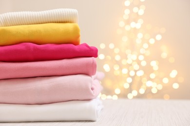 Photo of Stack of folded clothes on wooden table against beige background with blurred lights, space for text