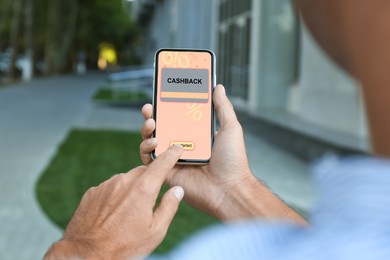 Image of Cashback. Man using smartphone outdoors, closeup. Illustration of credit card and percent signs on device screen
