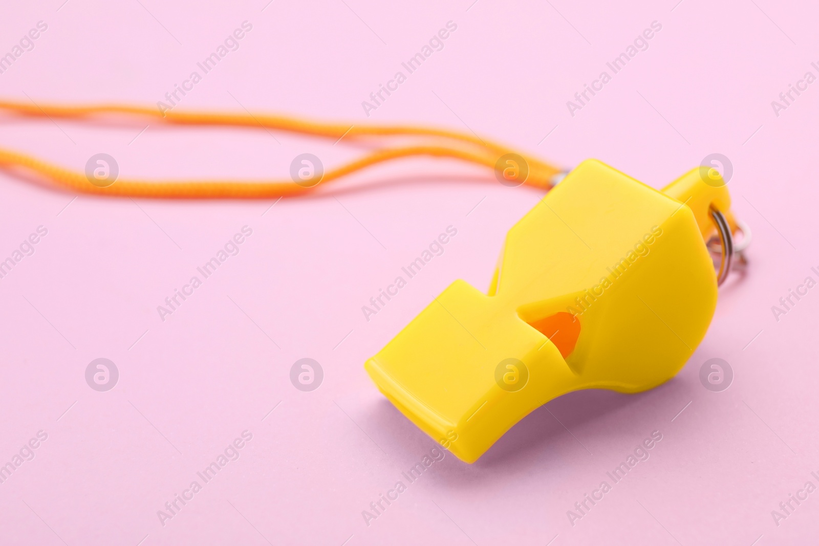 Photo of One yellow whistle with orange cord on pink background, closeup