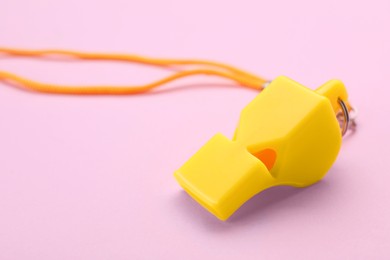 One yellow whistle with orange cord on pink background, closeup