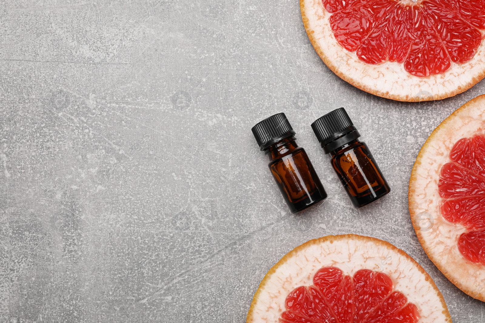 Photo of Bottles of essential oil with grapefruit slices on grey table, flat lay. Space for text