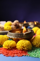Photo of Diwali celebration. Diya lamps, colorful rangoli and chrysanthemum flowers on blue table against violet background, closeup. Space for text
