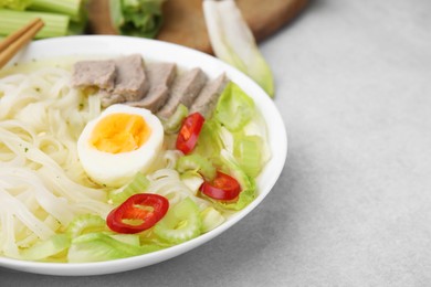 Photo of Bowl of delicious rice noodle soup with meat and egg on light grey table, closeup. Space for text