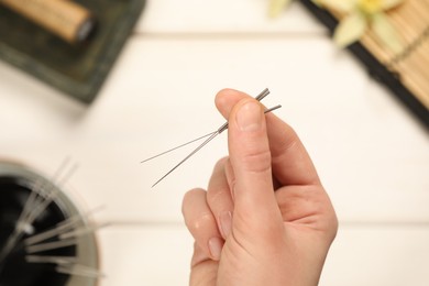 Photo of Woman holding many acupuncture needles over white wooden table, closeup