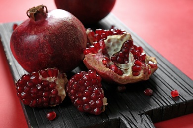 Photo of Wooden board with delicious ripe pomegranates on color background, closeup