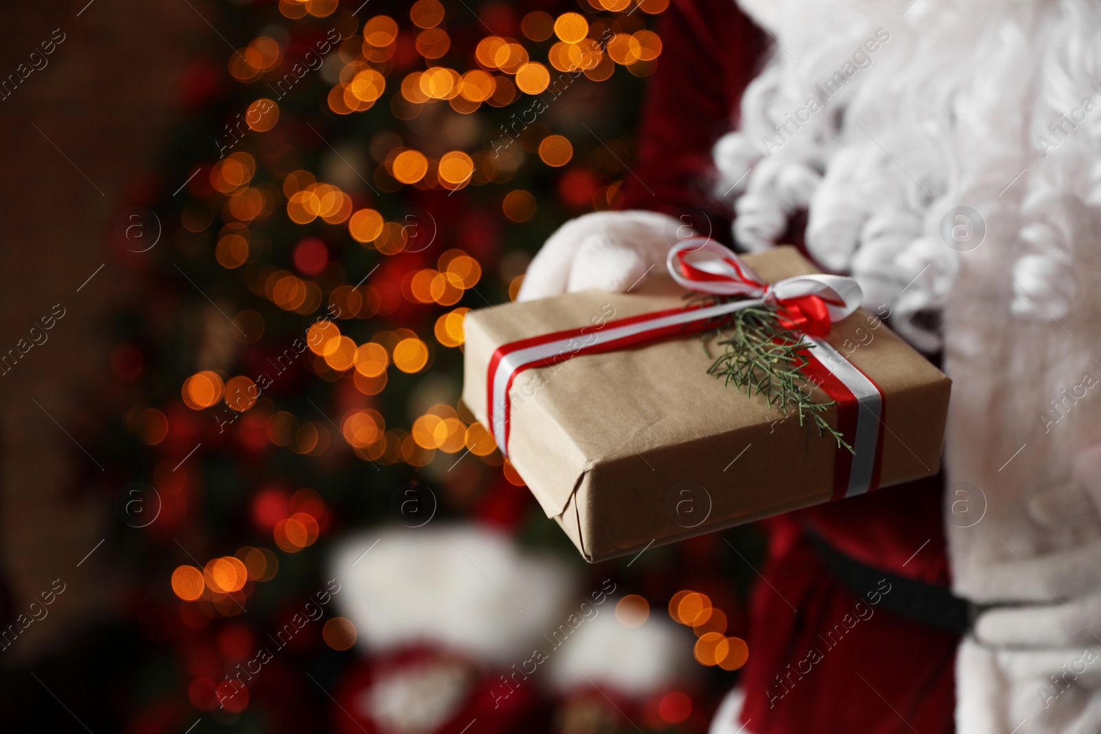 Photo of Santa Claus holding Christmas gift against blurred festive lights, closeup