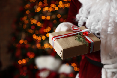 Santa Claus holding Christmas gift against blurred festive lights, closeup