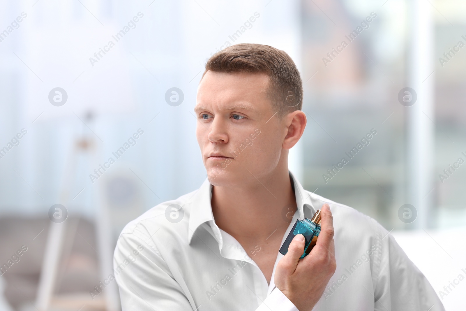 Photo of Handsome man in shirt using perfume on blurred background