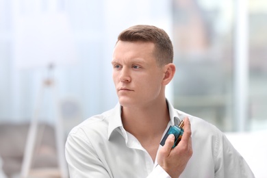 Photo of Handsome man in shirt using perfume on blurred background