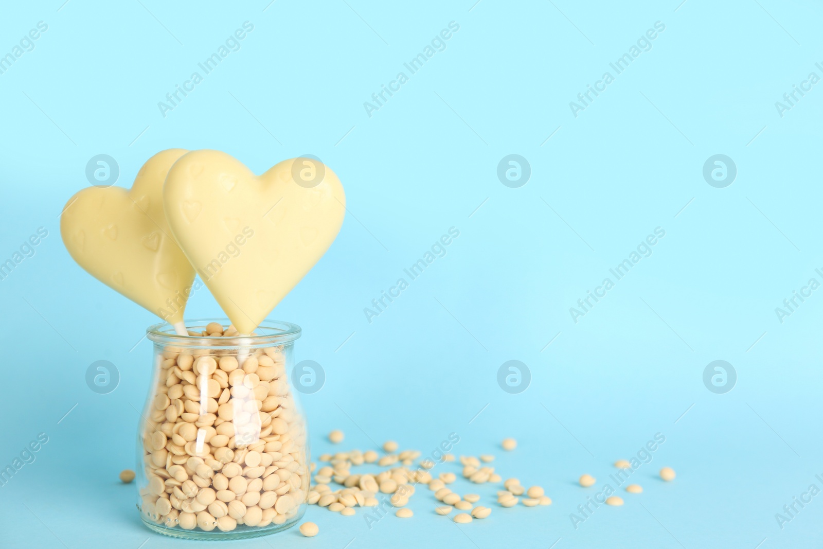 Photo of Chocolate heart shaped lollipops with chips in glass jar on turquoise background. Space for text