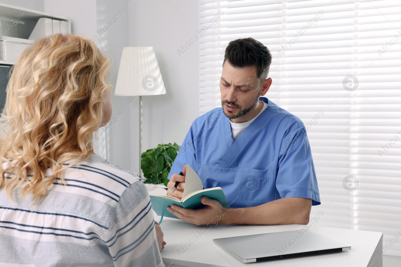 Photo of Doctor with notebook consulting patient at table in clinic