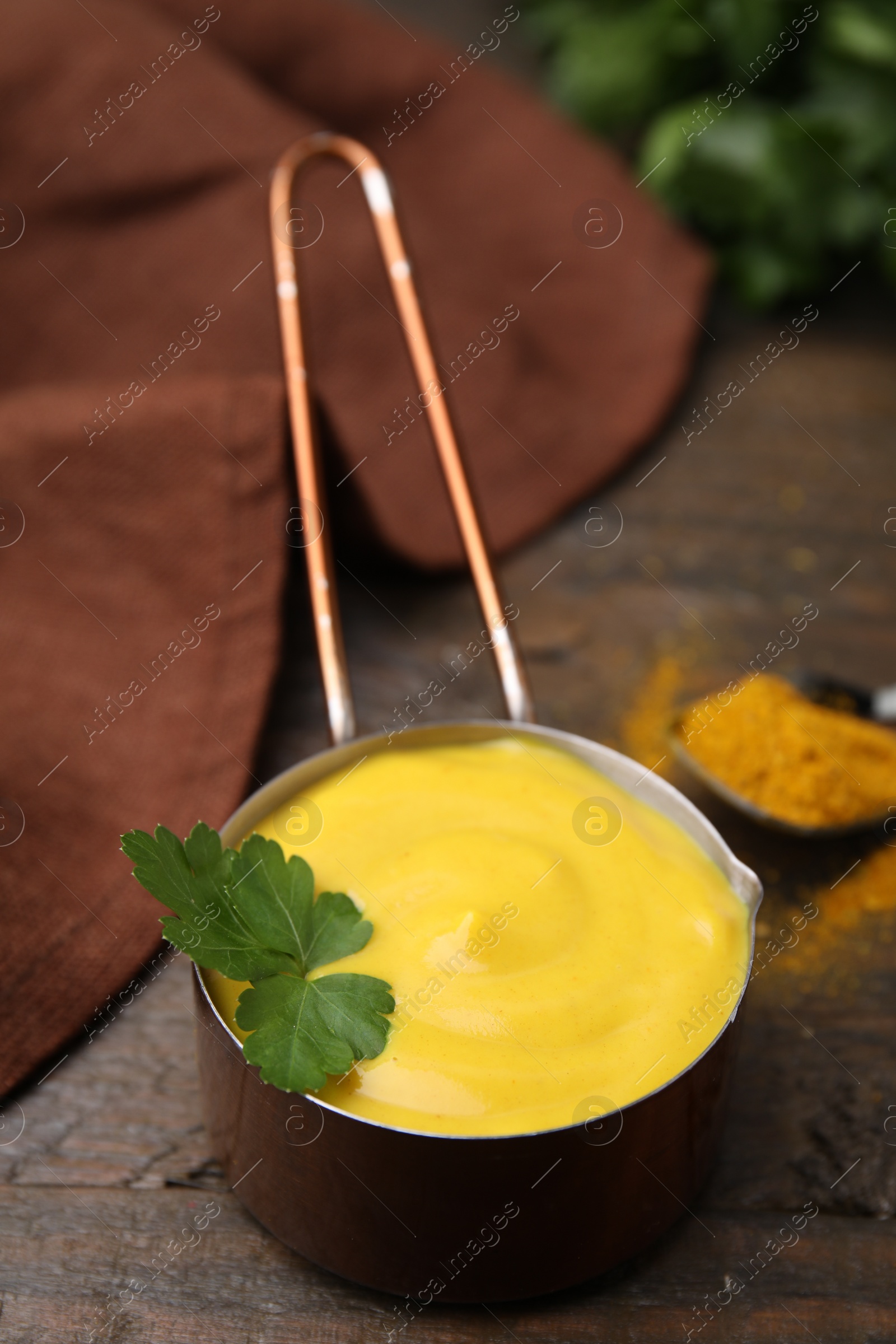 Photo of Saucepan with tasty curry sauce, powder and parsley on wooden table, closeup