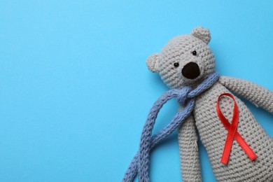 Cute knitted toy bear with red ribbon on blue background, top view and space for text. AIDS disease awareness