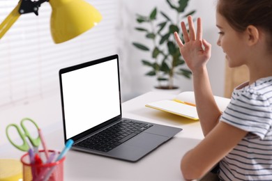 Photo of E-learning. Girl raising her hand to answer during online lesson at table indoors