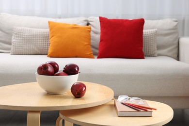 Photo of Red apples with book on nesting tables and comfortable sofa in living room. Interior design