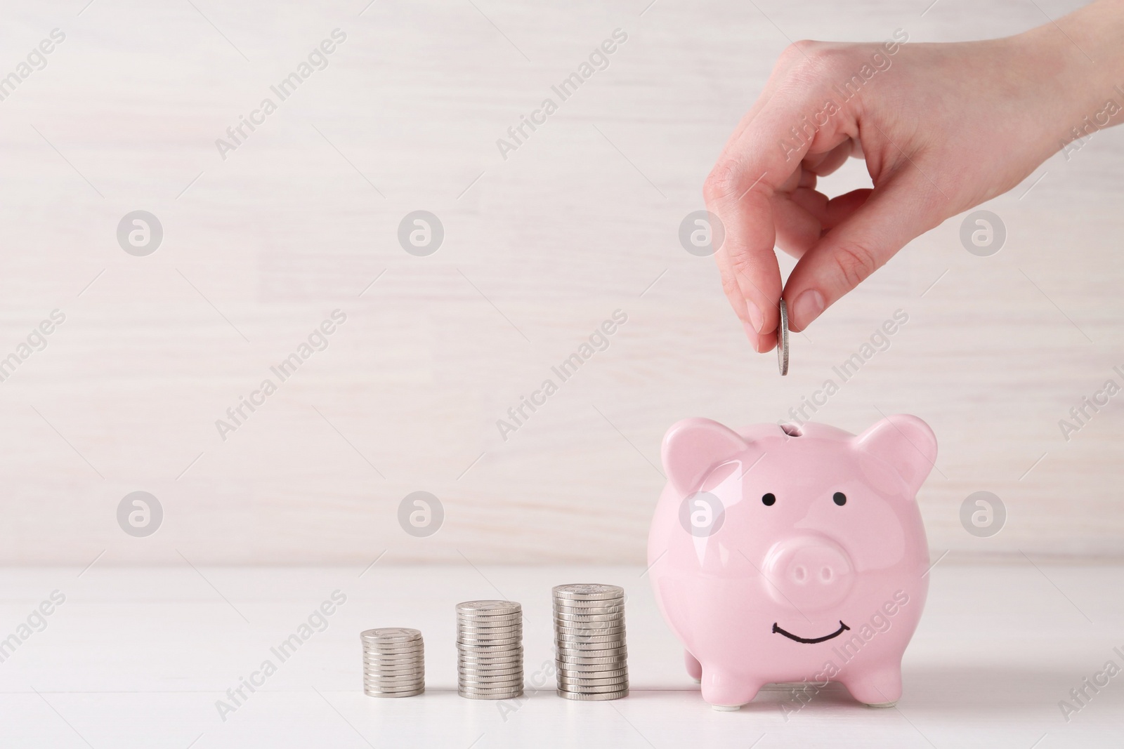 Photo of Financial savings. Woman putting coin into piggy bank at white wooden table, closeup. Space for text