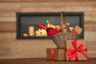 Photo of Wicker basket with bottle of wine and gift boxes on table in room. Space for text