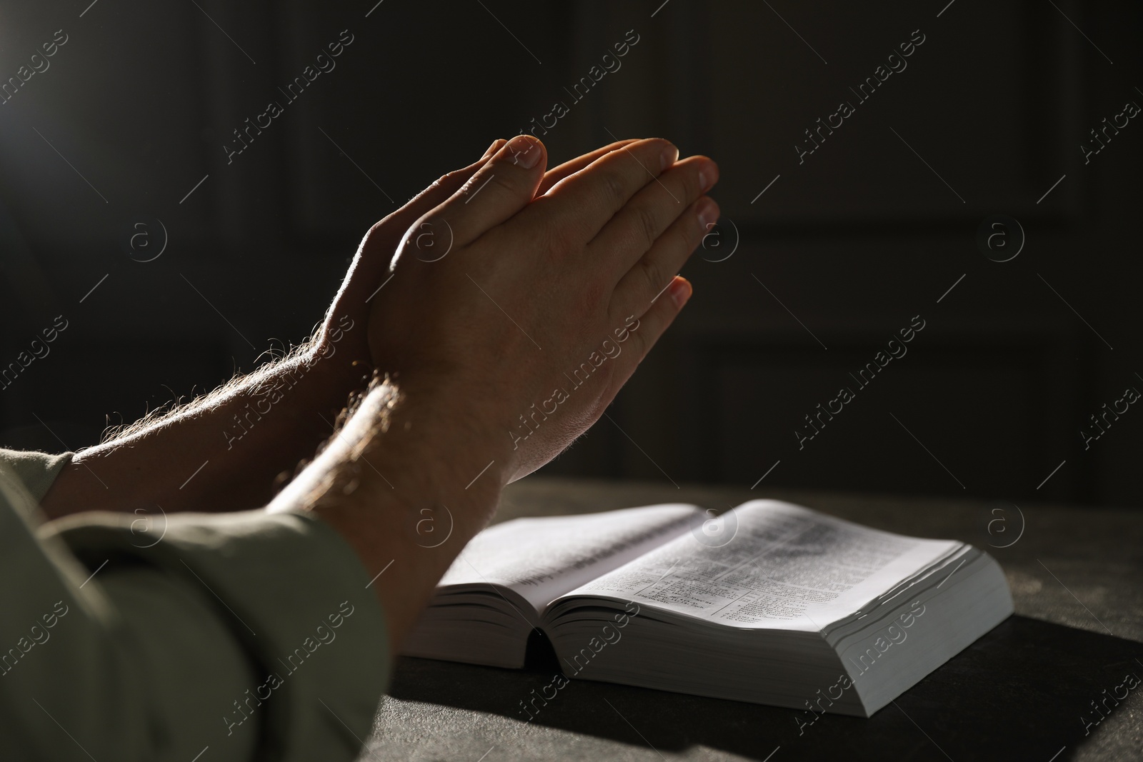 Photo of Religion. Christian man praying over Bible at table, closeup