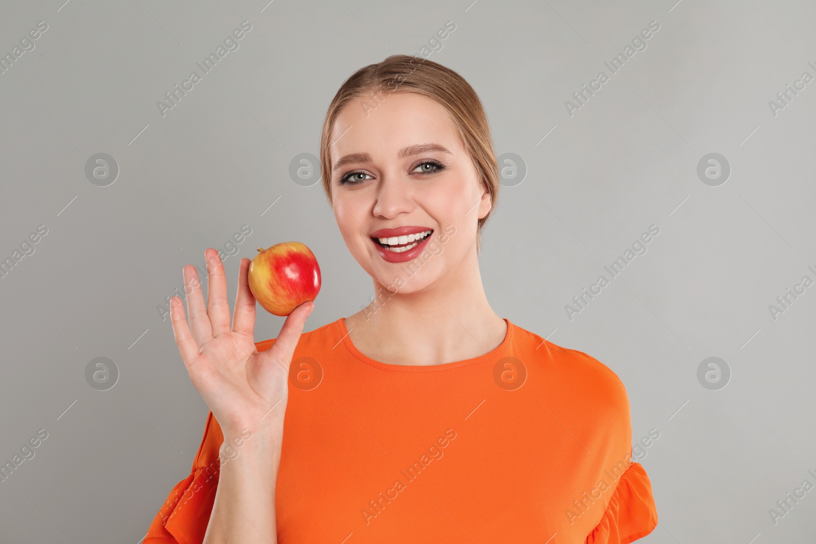 Photo of Young woman with apple on grey background. Vitamin rich food