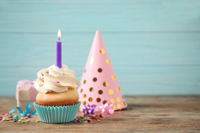Composition with birthday cupcake on wooden table against light blue background. Space for text