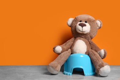 Teddy bear on light blue baby potty on stone table against orange background, space for text. Toilet training