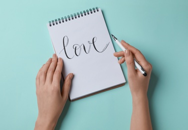 Photo of Woman writing word LOVE in notepad on turquoise background, top view