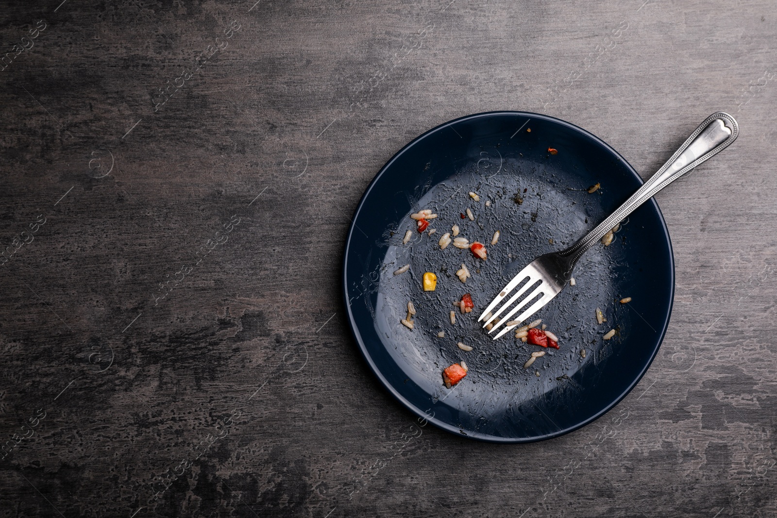 Photo of Dirty plate with food leftovers and fork on grey background, top view. Space for text