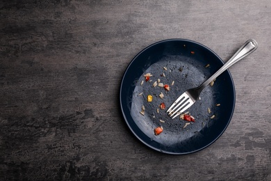 Photo of Dirty plate with food leftovers and fork on grey background, top view. Space for text