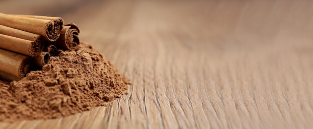 Cinnamon powder and sticks on wooden table, closeup view with space for text. Banner design