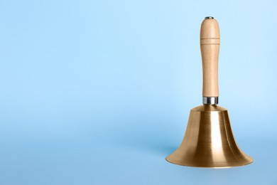 Photo of Golden school bell with wooden handle on light blue background. Space for text