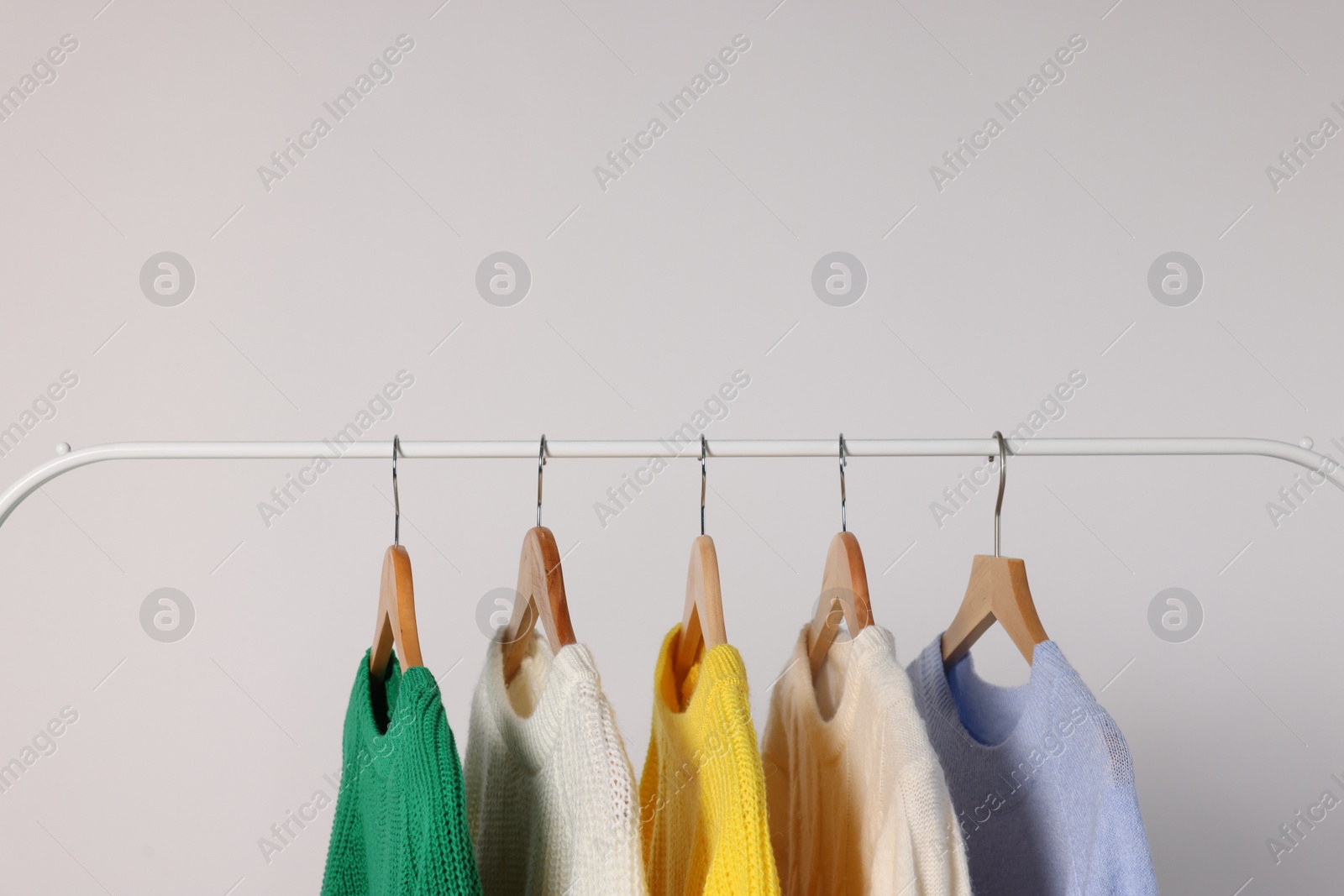 Photo of Rack with different warm sweaters on light background. Space for text