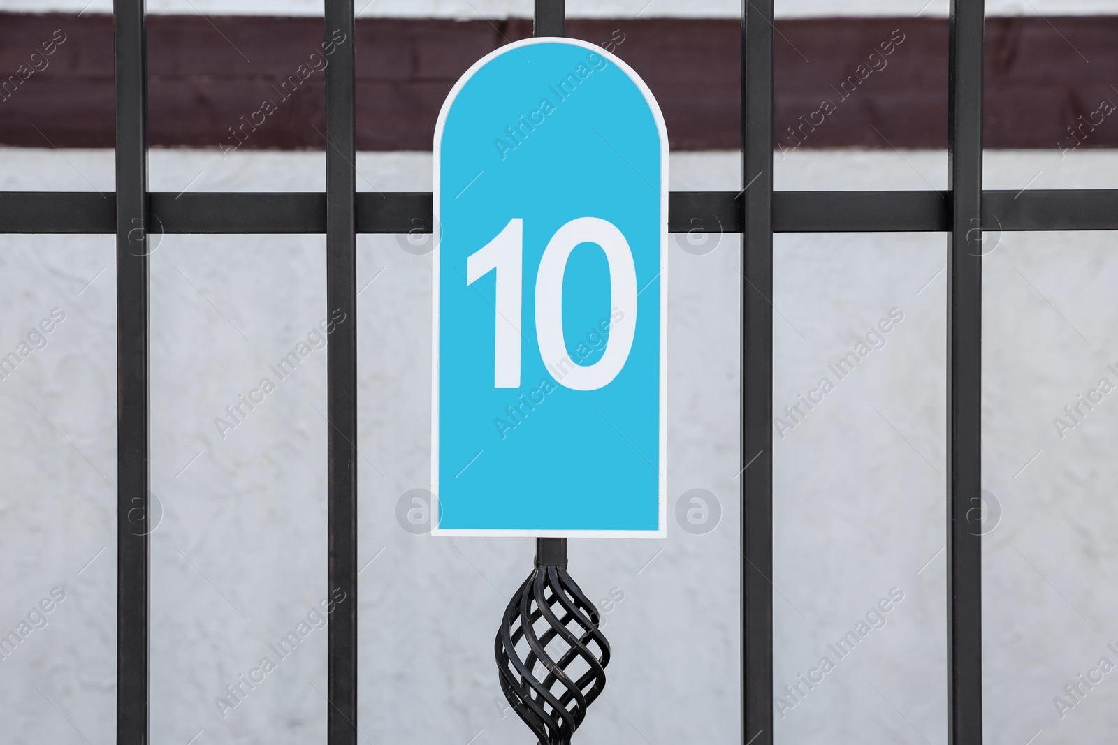 Photo of Plate with house number ten hanging on iron fence outdoors