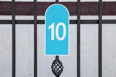 Photo of Plate with house number ten hanging on iron fence outdoors